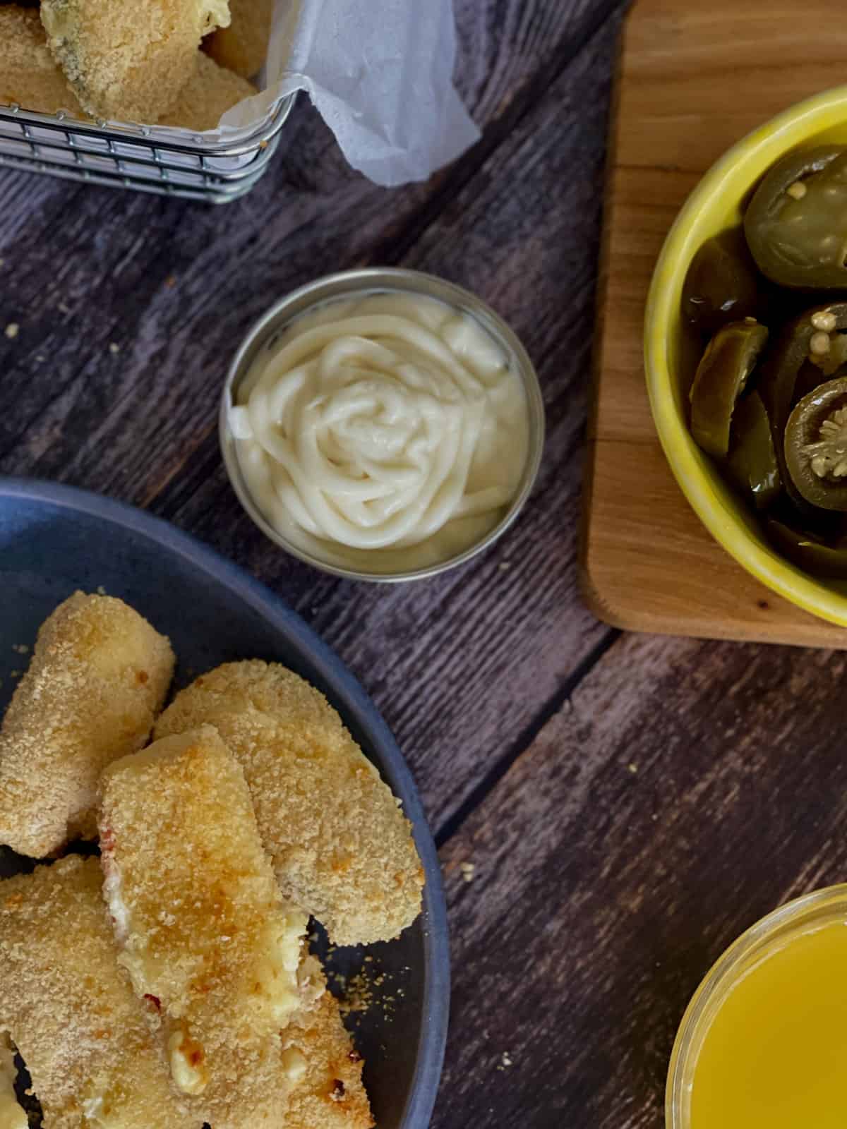 Birds Eye view of crispy golden jalapeño poppers served on a blue plate, with a creamy dip and sliced jalapeños.