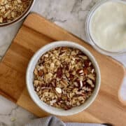 crispy air fryer granola served in a white bowl on a wooden board, with yoghurt.