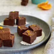 homemade dark chocolate orange-flavoured fudge garnished with a sprinkle of fresh orange zest, served on a dark blue plate.