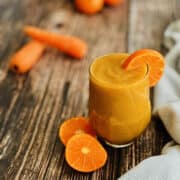 fresh apple, orange and carrot juice served with slices of orange on a wooden board.