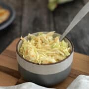 fresh coleslaw served in bowl on board with spoon.