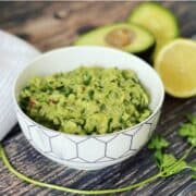 guacamole (smashed avocado dip) served in a bowl with lemons on the side.