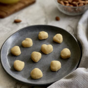 vegan marzipan candy in the shape of hearts and seashells, served on blue plate with almonds in the background.