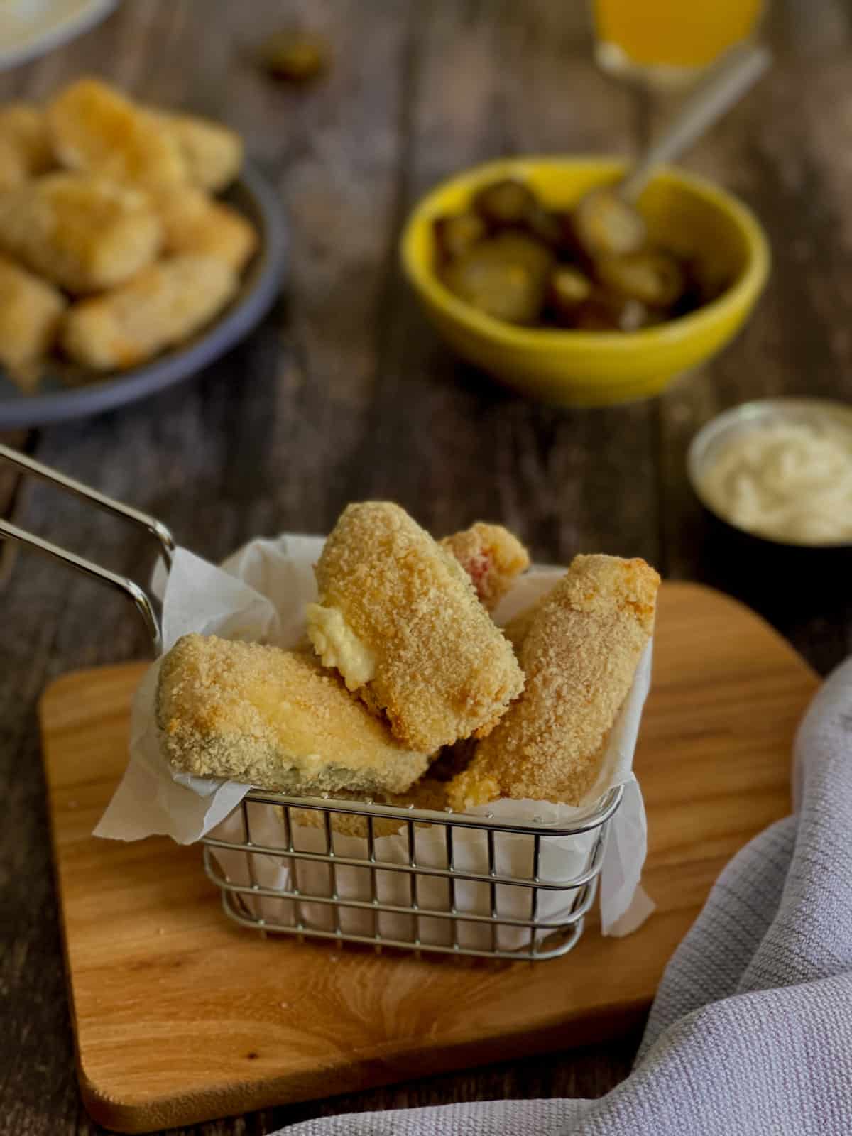 crispy and cheesy jalapeño poppers served in a basket on a board, next to a white cloth and a creamy dip.