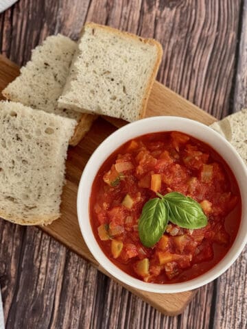 ratatouille with fresh basil on top, served in white bowl on wooden board, with fresh bread.