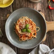Birds Eye image of Italian tomato spaghetti, garnished with cheese and fresh basil, served on a blue plate and wooden board.