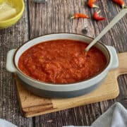 tomato spaghetti sauce in serving dish with spoon, on a wooden board.