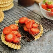 pizzelles covered with smooth chocolate spread and sliced fresh strawberries, placed on cooling rack.