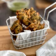 crispy spinach onion pakora served in basket with chutney.
