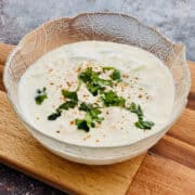 cucumber raita for biriyani served in bowl on board, garnished with fresh coriander/cilantro.
