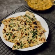 garlic naan made without yeast, garnished with coriander, served on a white plate.