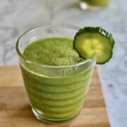 green kale cooler smoothie in glass with cucumber served on wooden board.