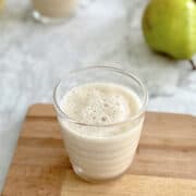 fresh pear juice served in glass on wooden board, pear in background.