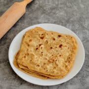 stack of golden plain parathas (Indian flatbreads) served on a white plate.