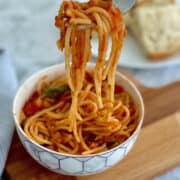 vibrant ratatouille spaghetti in a white bowl, lifted by fork.