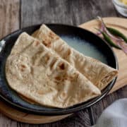 fresh homemade vegan roti served on plate with lentils/daal in background.