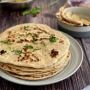 stack of wholewheat naans served on plate, lentils and onions in background.