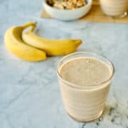 banana date smoothie served in glass, bananas and walnuts in background.