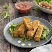 crispy golden air fryer paneer fingers served on a blue plate with Indian mint sauce, chutneys and salad.