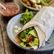 paneer wrap filled with paneer, salad leaves and dips, served on a blue plate, with dips and paneer in background.