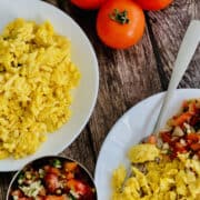 fluffy scrambled eggs made without milk, served on plates with salsa and fresh tomatoes on the vine in the background.