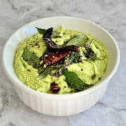 green coconut coriander chutney served with tempering in a white dish.