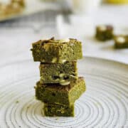 green matcha brownies with white chocoalte chips stacked on top of each other on plate.