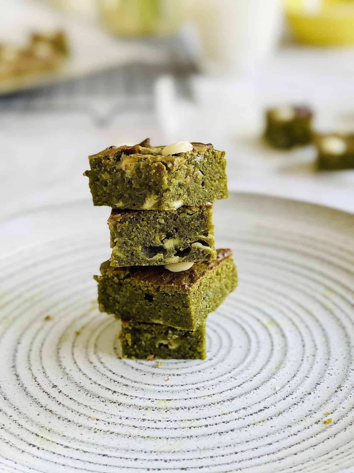 green matcha brownies with white chocoalte chips stacked on top of each other on plate.