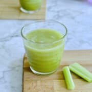 organic green celery juice served in glass on board, with celery sticks on the side.