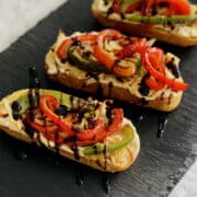 Mediterranean bruschetta with caramelized onions, roasted peppers and hummus - topped with a drizzle of balsamic glaze, served on a black board.