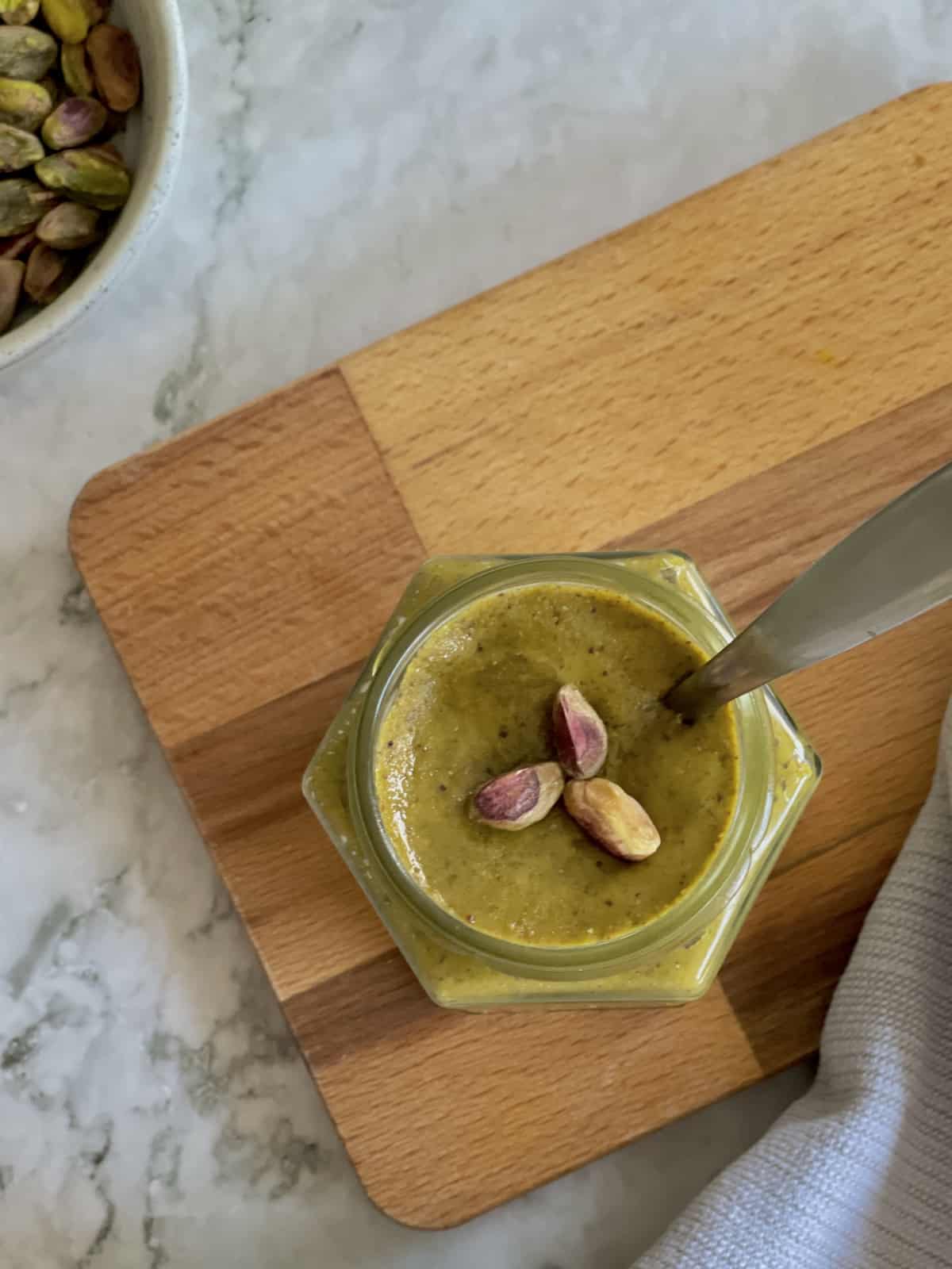 birds eye view of pistachio paste in jar, decorated with 3 pistachios on top.