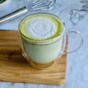 matcha (green tea) latte served in transparent cup, on board.