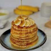 stack of almond flour banana pancakes drizzled with warm maple syrup, topped with sliced bananas.
