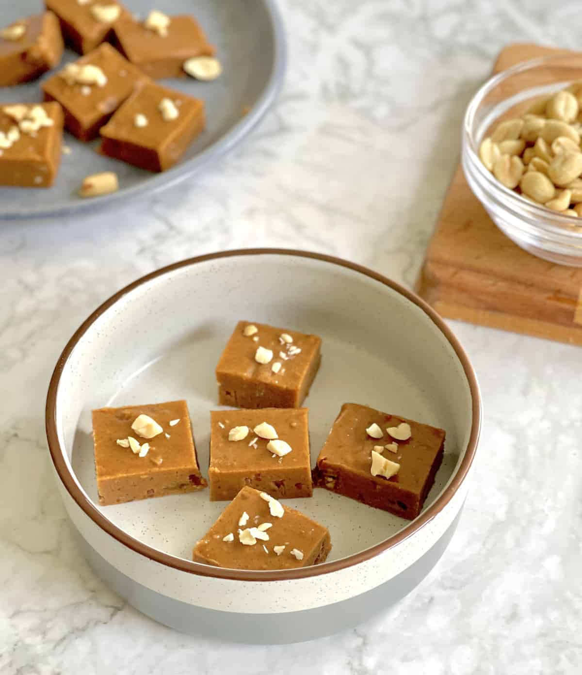 peanut butter fudge squares, with fudge pieces and a bowl of peanuts in the background.