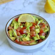 avocado pico de gallo in a bowl with sliced lemon in the background.