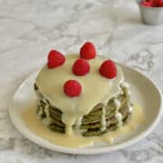 close up of stacked matcha pancakes, topped with white chocolate ganache and fresh raspberries.