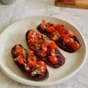 three slices of purple sweet potato bruschetta on a white plate.