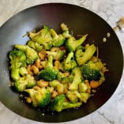 garlic broccoli and cashew stir fry in wok, garnished with sesame seeds.