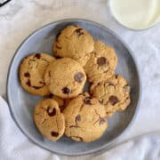 close up of freshly baked oat chocolate chip cookies on blue plate, with a glass of milk.