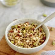 close up of air fryer pistachio and rose granola in bowl on wooden board.