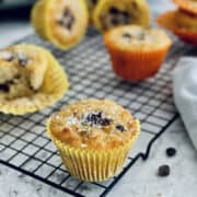 close up of golden coconut flour chocolate chip muffins, topped with coconut flakes, on a wire rack.