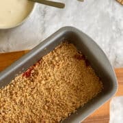 hero image of golden rhubarb crumble in serving dish, with cream on the side.
