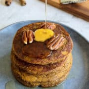 stacked pumpkin pancakes topped with melted butter, maple syrup and pecan nuts.