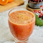 vibrant orange and cranberry juice served in a glass, with festive ornaments and decorations in background.