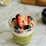 vibrant matcha overnight oats served in a glass, topped with a layer of creamy yogurt, fresh strawberries, blueberries and flaked almonds.