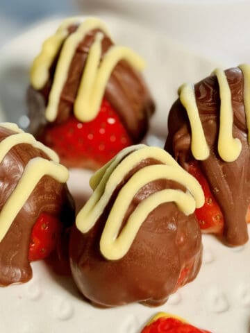 chocolate covered juicy strawberries drizzled with melted white chocolate, served in a plate.