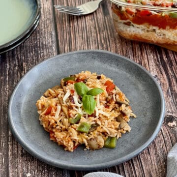 Italian mushroom rice served on a blue plate, topped with cheese and basil leaves, with layered Italian rice in background.