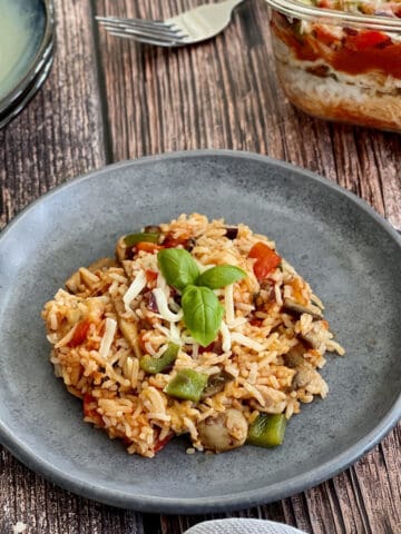 Italian mushroom rice served on a blue plate, topped with cheese and basil leaves, with layered Italian rice in background.