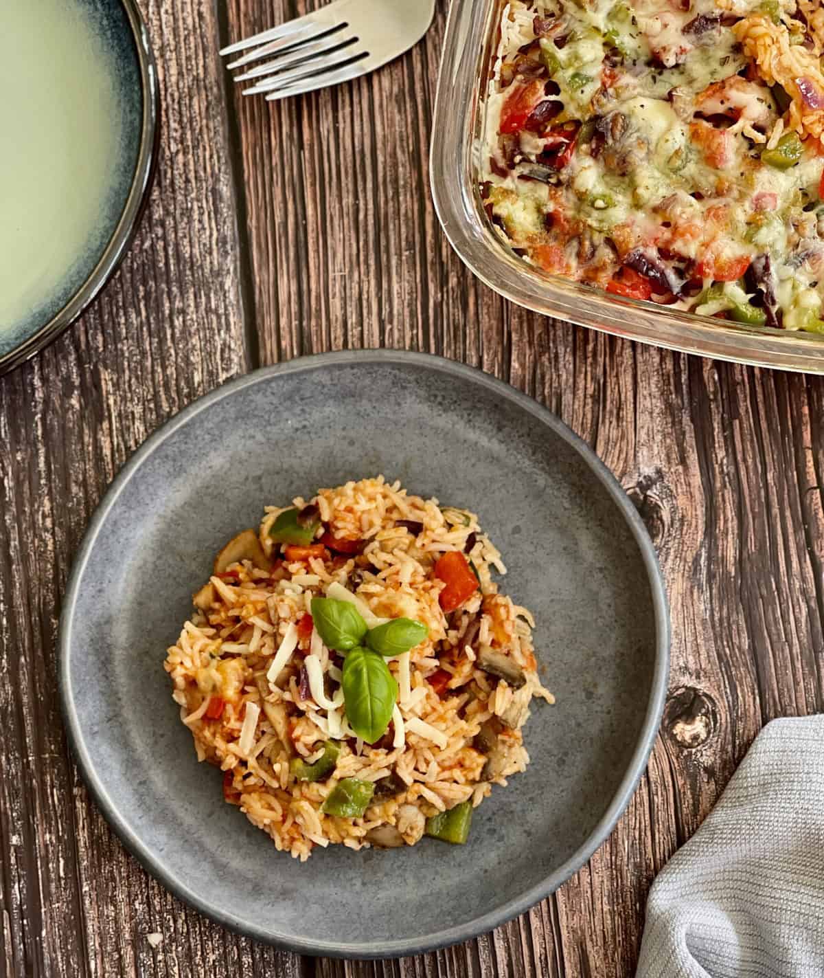 tomato, mushroom and vegetable rice served on a blue plate, topped with cheese and basil leaves.