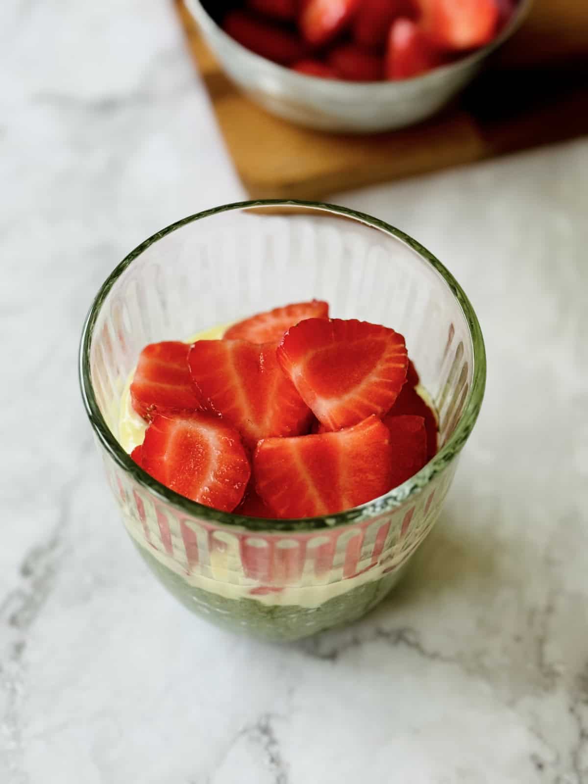 creamy matcha chia seed pudding with a layer of white chocolate and sliced strawberries, served in a glass.